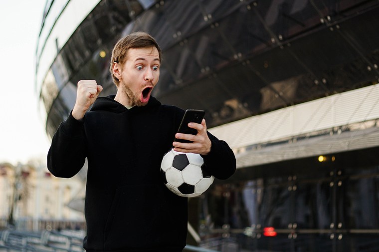 Man betting on smartphone outside football stadium